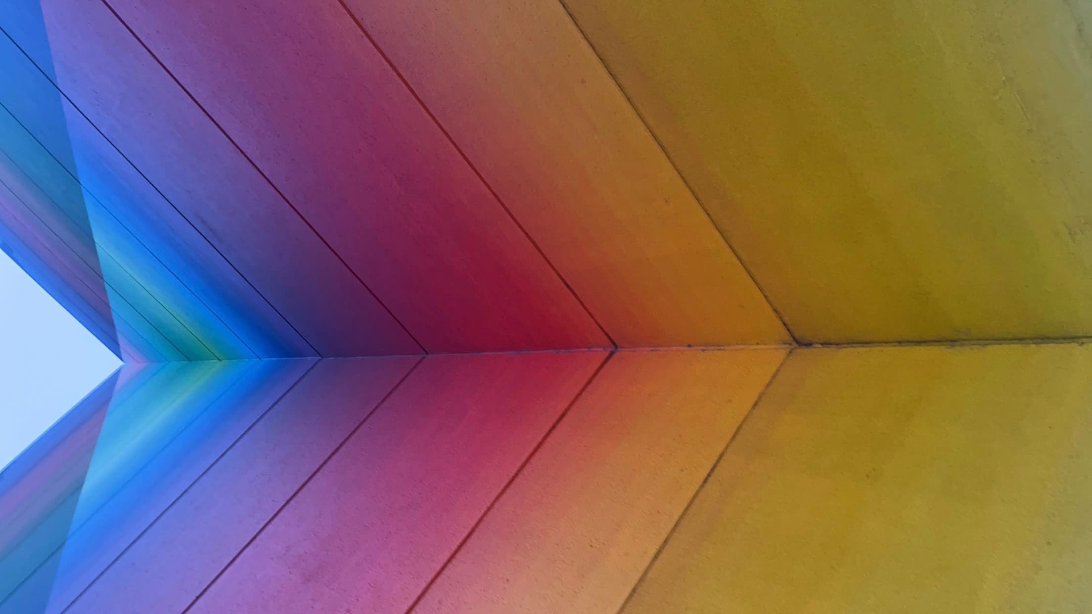 Rainbow-colored wooden panels meeting at a sharp angle, creating a vibrant and colorful geometric perspective.