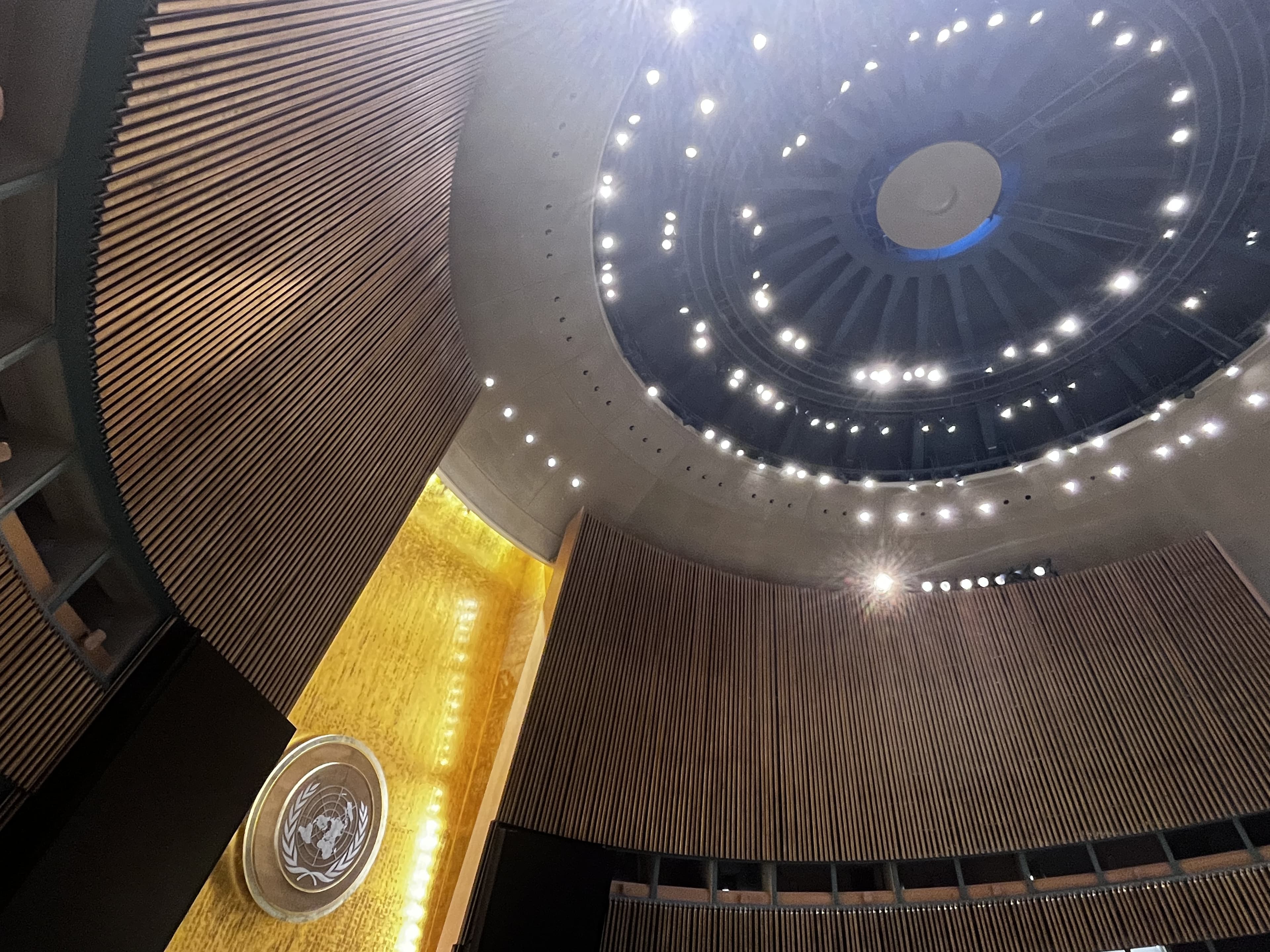 United Nations General Assembly hall interior with gold emblem wall and circular domed ceiling.